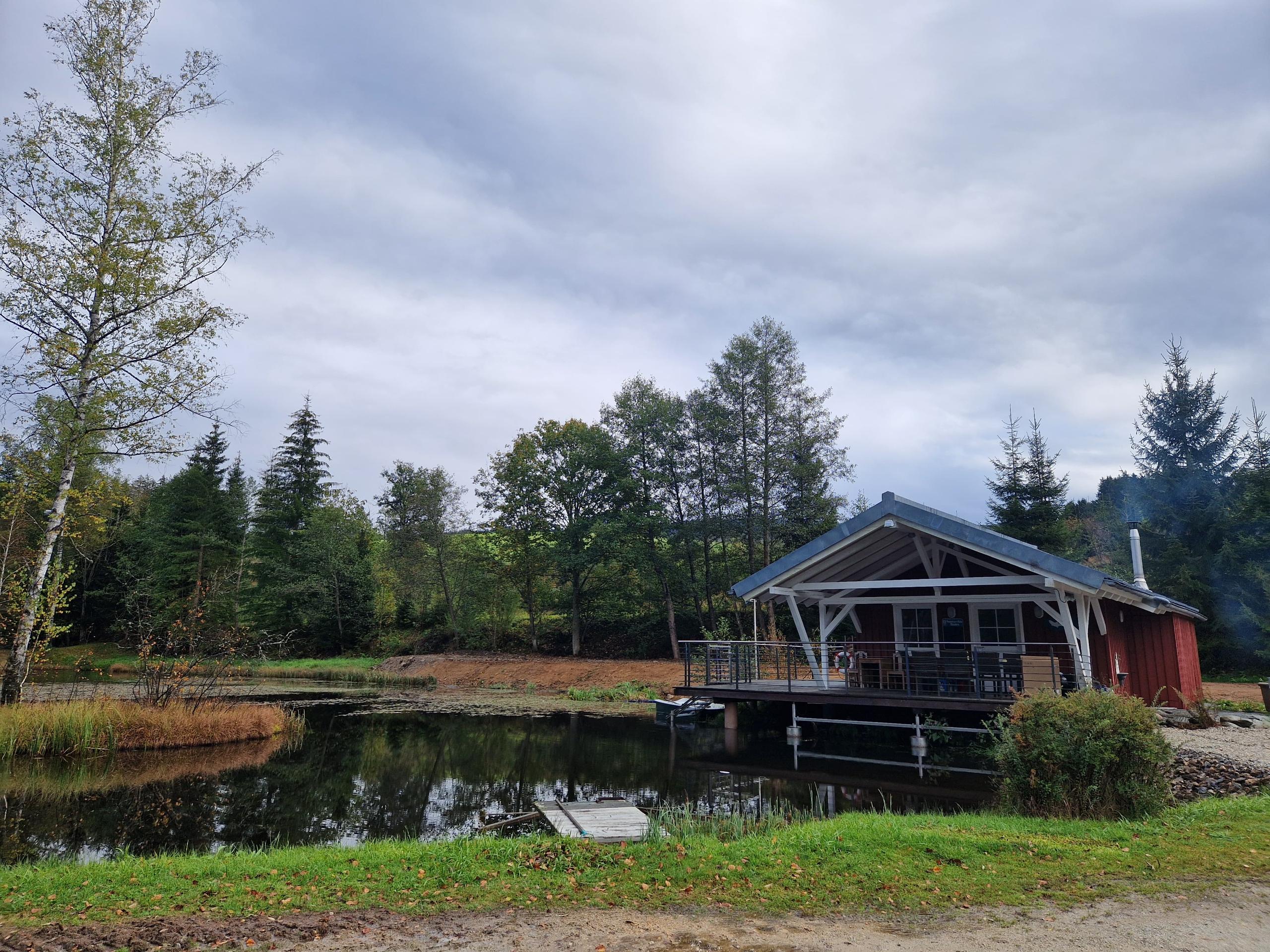 Fischteisch mit Insel, im Hintergrund Holzhütte mit Überdachung